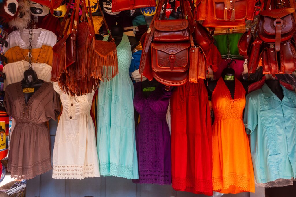 A lively display of colorful dresses and leather bags at a bustling market stall, showcasing fashion diversity.